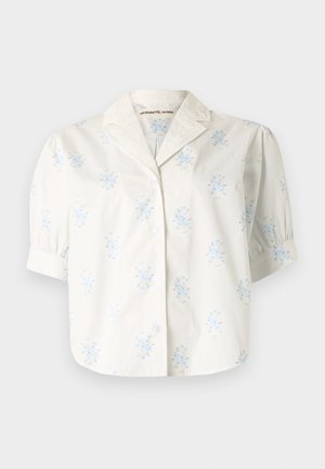 Blouse blanche à manches courtes avec imprimés floraux bleus, devant boutonné, manches bouffantes et col cranté avec une broderie subtile.