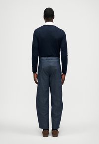 Jūras spēku zīmola džemperis un gaiši zila džinsa bikses ar brīvu piegriezumu. Biksēm ir aizmugurējās kabatas un vienkārša jostas dizains.