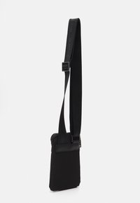 Sac à bandoulière noir avec fermeture éclair, fabriqué en tissu durable. Présente une bandoulière tissée et un accent en cuir lisse à l'avant.