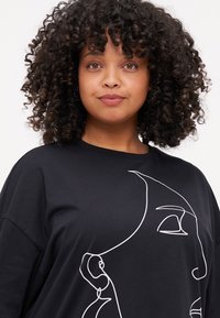 Svart t-skjorte laget av myk stoff, med en kontinuerlig hvit linjetegning av et ansikt foran. Løs passform med vide ermer.