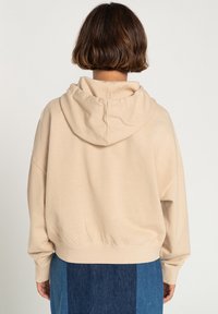Beige, oversized hættetrøje med hætte og ribbet kant. Fremstillet i blødt bomuldsmateriale med sænket skulderdesign. Glat tekstur, minimal detaljer.