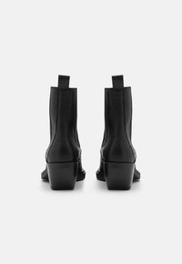 Černé kotníkové boty vyrobené z texturované kůže, s blokovým podpatkem a poutkem na zadní straně. Elegantní, minimalistický design s hladkými liniemi.