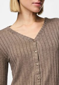 Brun ribbad långärmad topp med V-ringning och fem knappar framtill. Materialet verkar texturerat med horisontella ränder.