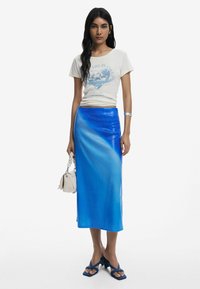 Blauwe satijnen kokerrok met een verloopafwerking, gecombineerd met een licht graphic t-shirt. Accessoires zijn een kleine handtas en blokhak sandalen.