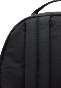 Mochila negra con un exterior de tejido suave, correas de hombro acolchadas y un asa en la parte superior. Detalles de costura a lo largo de las costuras.