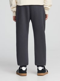 Pantaloni della tuta grigio scuro in tessuto morbido, caratterizzati da una vestibilità ampia e polsini elasticizzati, abbinati a sneakers nere e bianche.