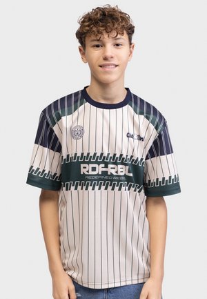 Dreng med krøllet hår iført en hvid og mørkegrønstribet RDE RBL sportst-shirt, stående mod en ensfarvet lys baggrund.