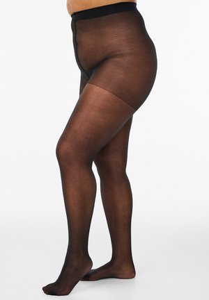 Jalad, mis kannavad läbipaistvaid musti sukkpükse tugevdatud kõrge vöö ja reieosadega, seisavad tavalise valge tausta ees.