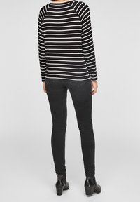 Schwarz-weiß gestreiftes Langarmshirt mit Raglanärmeln, kombiniert mit schwarzen engen Jeans und kniehohen Stiefeletten, von hinten betrachtet.