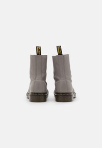 Botas de tobillo de cuero gris con tiradores amarillos, suela negra y detalle de costura visible. Diseño clásico de punta redonda con textura sutil.