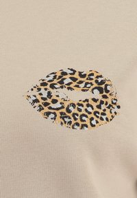 Tessuto beige con design labbra a stampa leopardata in nero, con accenti oro e argento, caratterizzato da una superficie testurizzata.