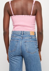 Top ajustado rosa con textura fruncida y tirantes finos, combinado con unos vaqueros de denim azul claro de cintura alta con una etiqueta en la parte trasera del cinturón.