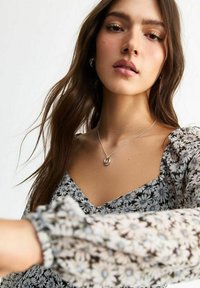 Blommig klänning med v-ringning, prydd med små prästkragar i vitt och blått på en mörk bakgrund. Silverhalsband med en cirkulär berlock.