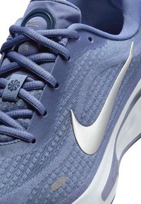 Scarpa da ginnastica viola con materiale testurizzato, caratterizzata da un logo swoosh bianco, accenti grigi e lacci coordinati, in una vista ravvicinata.