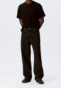 Zwart T-shirt met een ronde halslijn, gecombineerd met zwarte, wijde jeans met hoge taille. De jeans hebben steekzakken aan de voorkant en subtiele stiksels.