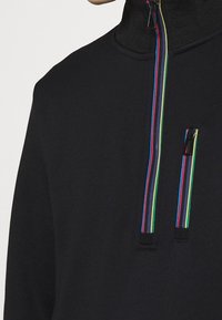 Sweat-shirt zippé noir avec un col haut et des fermetures éclair colorées en rouge, vert, bleu et jaune ; détails de tissu texturé sur les épaules.