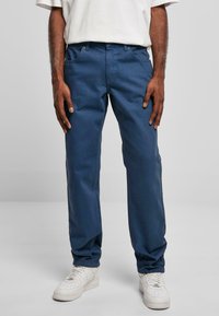 Pantalons en coton bleu avec une coupe droite, dotés de cinq poches, de passants de ceinture et d'une fermeture éclair. Associés à des baskets blanches.