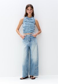 Ljust blå denimcroppad topp med texturerade vertikala veck, parat med vida ljusblå jeans med en lätt blekning och sömdetaljer.