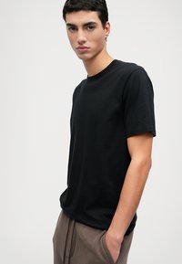 Svart bomulls t-shirt med rund hals och korta ärmar, med en avslappnad passform och en mjuk textur mot en neutral bakgrund.