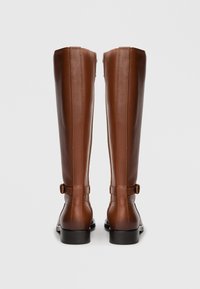 Bottes hautes en cuir marron à finition lisse, avec une fermeture éclair latérale, un bout arrondi et un détail de boucle sur la bride de la cheville.