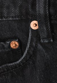 Μαύρο τζιν ύφασμα με εμφανείς ραφές, που διαθέτει δύο χαλκόχρωμους καρφίτσες στην περιοχή μιας τσέπης.