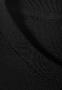 Tela de camiseta de algodón negra con una textura suave que presenta un cuello acanalado. La costura es limpia y uniforme en toda la prenda.