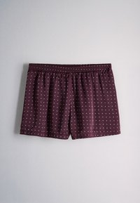 Maroon shorts with small white polka dots and an elastic waistband hanging against a plain light gray background.