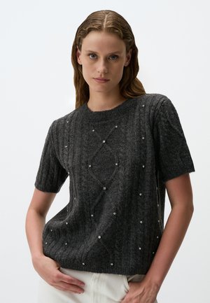 Pull gris à manches courtes en tricot côtelé, présentant des motifs en diamant et de petites gemmes décoratives disséminées. Encolure ras du cou et coupe décontractée.