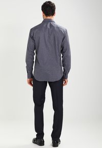 Mörkblå rutigt skjorta med knäppkrage, långa ärmar och rundad nederkant, tillsammans med mörka byxor och svarta skor.