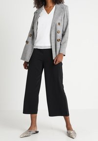 Blazer double boutonné à carreaux gris avec des boutons dorés, associé à un haut blanc en V, un pantalon noir à jambes larges et des ballerines à imprimé serpent.