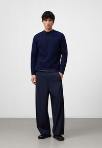 Maglione navy con motivo a righe testurizzate, colletto rotondo, abbinato a pantaloni navy a gamba larga e scarpe nere basse. Design attento ai dettagli.