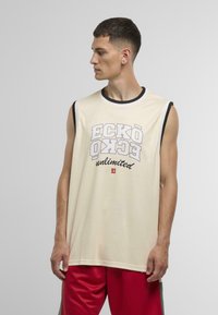 Ujjatlan krémszínű tank top fekete díszítéssel és merész "ECKO unlimited" grafikai mintával szürkében és vörösben. Vörös rövidnadrággal viselve.