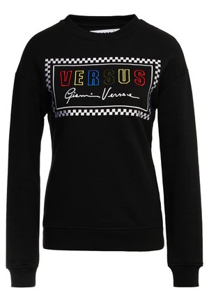 Musta crewneck-huppari, jossa monivärinen "VERSUS"-teksti ja Gianni Versacen allekirjoitus mustavalkoisessa ruudullisessa suorakaiteenmuotoisessa kehyksessä.