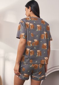 Gråt bomuldspyjamasæt med et gentaget mønster af brune Highland-køer, kortærmet top med rund hals og matchende shorts.