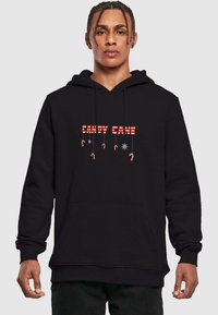 Čierna mikina s kapucňou s nápisom "CANDY CANE" v červených a bielych pruhovaných písmenách, so grafikou cukrovej palice a snehovými vločkami nižšie, s predným klokankovým vreckom.