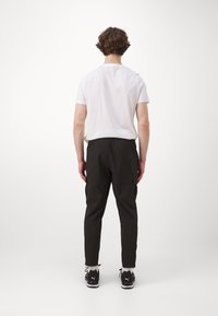Sorte cargo bukser med elastisk talje, sidelommer og tapered ben, parret med en simpel hvid T-shirt og sorte sportsko.