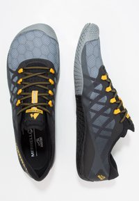 Scarpe leggere nere e grigie con un motivo esagonale, lacci gialli e una suola in gomma testurizzata per grip e stabilità.