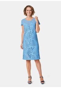 Hellblaues Kleid mit Spitze im Blätterdesign, kurzen Ärmeln und knielanger Schnitt. Getragen mit passenden blauen Sandalen.