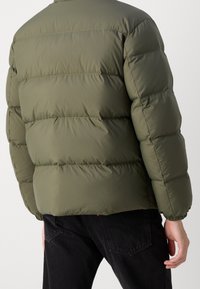 Olivgrön puffjacka med quiltade sektioner, elastiska ärmslut och hög krage, sedd bakifrån. Slät, vattentåligt material.