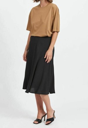 T-shirt oversize marron, jupe midi fluide noire et sandales à talons ouverts noires, sur fond neutre.
