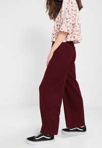 Burgundyfärgade vida byxor som matchas med en blommönstrad kortärmad topp. Svarta sneakers kompletterar looken med vita detaljer.