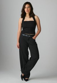 Svart halterneck crop top tillsammans med högmidjade vida svarta jeans och ett svart bälte. Jeans har diskreta sidoslitsar. Svarta klackar fulländar looken.