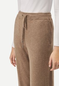 Bruna stickade joggingbyxor med dragsko i midjan, utrustade med sidofickor och mjuk textur. Tyget verkar varmt och mysigt.