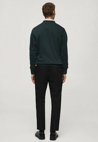 Felpa verde scuro con colletto rotondo, abbinata a pantaloni neri affusolati e scarpe nere. Tessuto liscio, design minimalista.