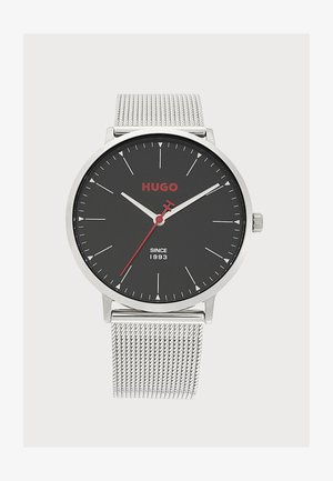Montre-bracelet à bracelet en maille argentée avec cadran rond noir, aiguilles blanches des heures et des minutes, aiguille des secondes rouge, et logo rouge "HUGO".