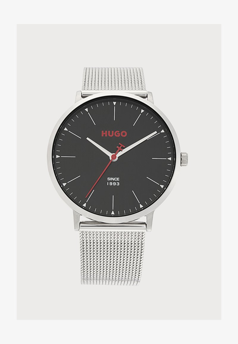 Montre-bracelet à bracelet en maille argentée avec cadran rond noir, aiguilles blanches des heures et des minutes, aiguille des secondes rouge, et logo rouge "HUGO".