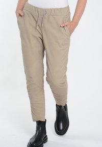 Beige elastische tailleband broek met trekkoord, taps toelopende pijpen, zijzakken en subtiele textuur, gecombineerd met zwarte enkellaarsjes.