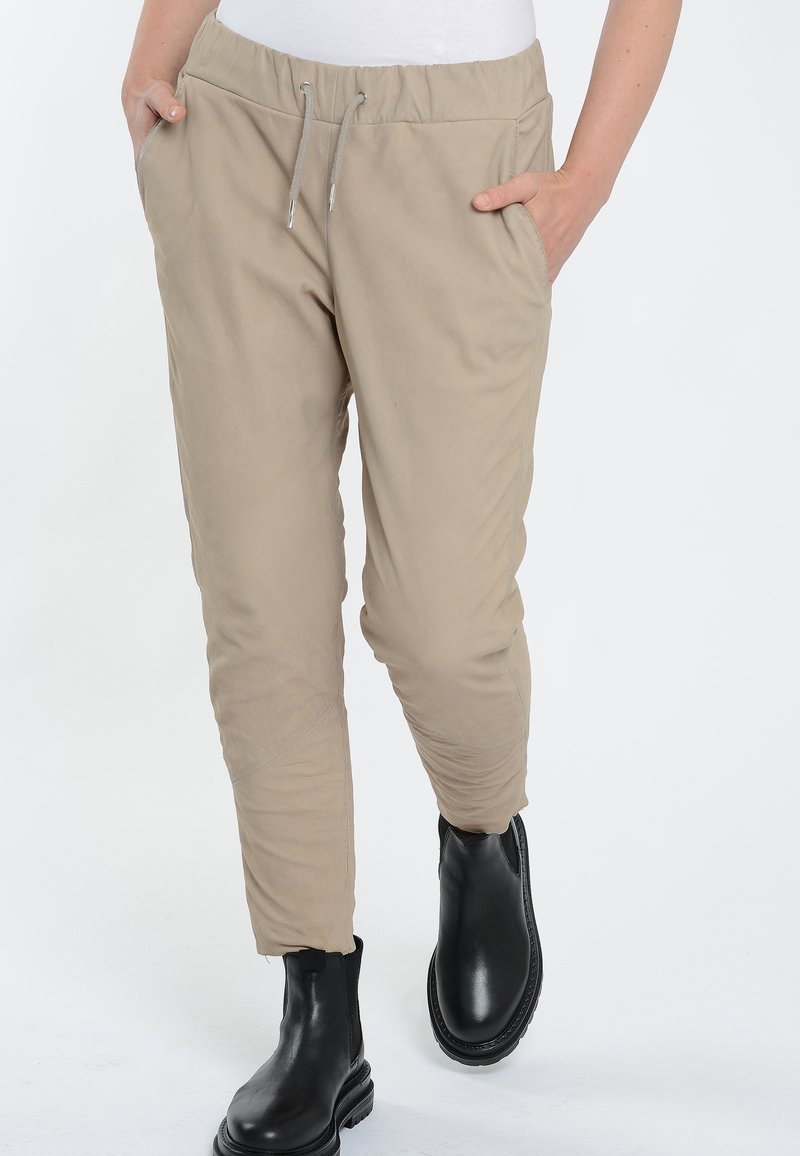 Beige elastische tailleband broek met trekkoord, taps toelopende pijpen, zijzakken en subtiele textuur, gecombineerd met zwarte enkellaarsjes.