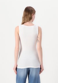 Top sin mangas blanco de canalé con escote redondo y un diseño ajustado. La textura de la tela es suave y ligera.