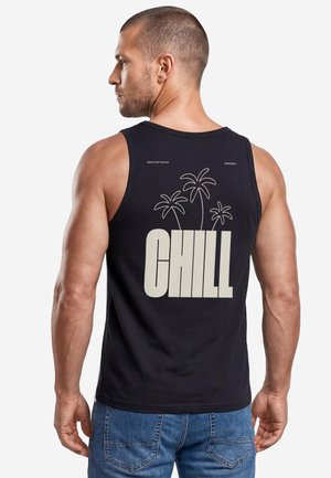 Man in black sleeveless shirt with palm tree design and large word "CHILL" on back, wearing blue jeans, facing left.